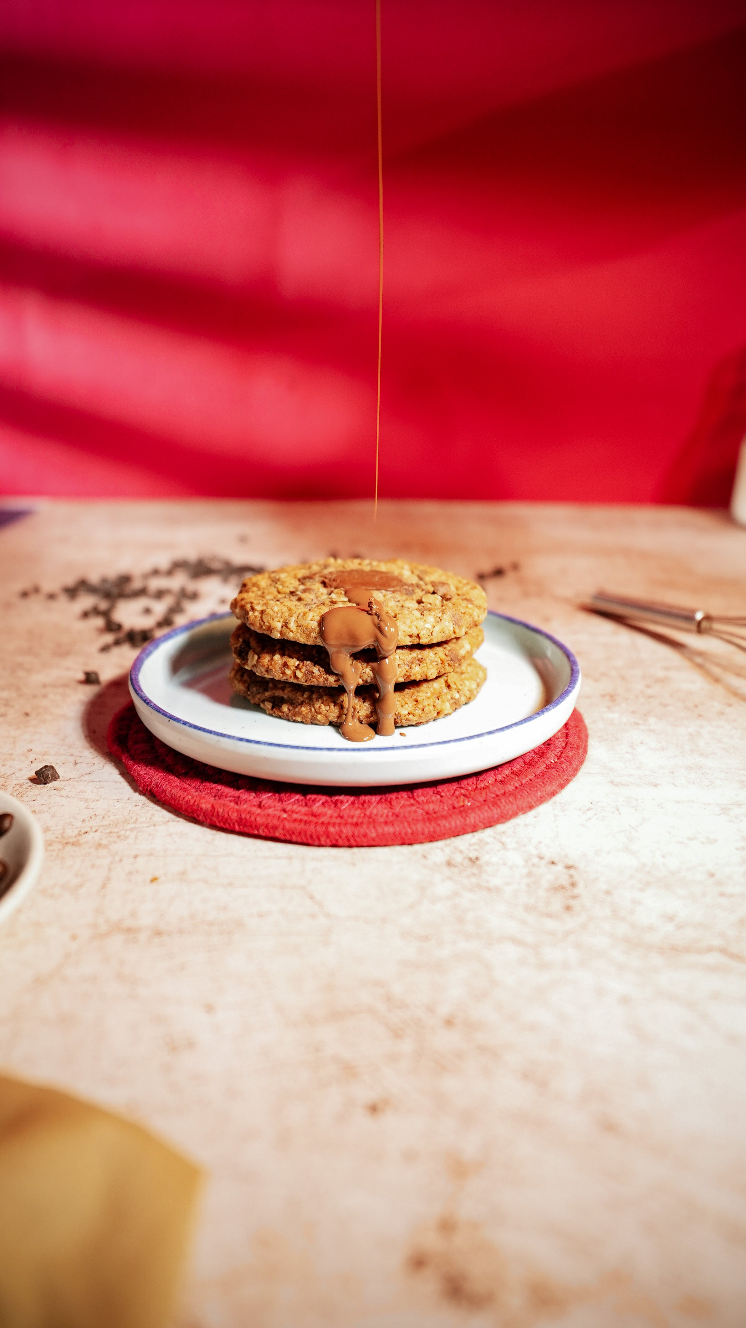 A stack of three oat chocolate chip cookies on a small plate, with melted chocolate drizzled over the top.