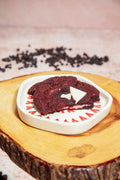 A deep red velvet cookie broken in half on a white plate, revealing its white chocolate filling and topped with a shard of white chocolate.